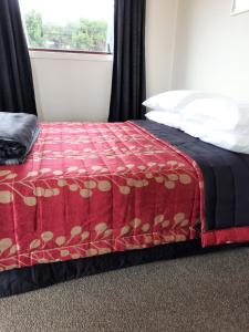 a bedroom with a bed with a red blanket and a window at Glenavys Waitaki River Motor Camp in Glenavy