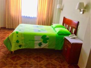 a bed with a green comforter with a phone on it at Hostal Residencial Lino in Huaraz