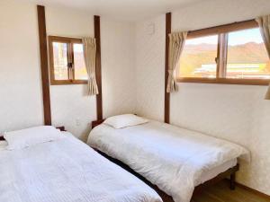 2 Betten in einem Zimmer mit 2 Fenstern in der Unterkunft 富士晴 Guest House in Minamitsuru