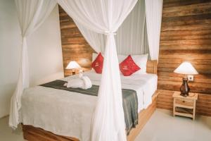 a bedroom with a bed with white curtains and red pillows at Mertasari Bungalows in Nusa Penida