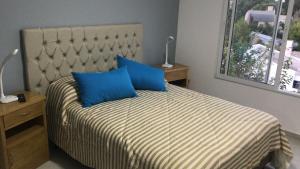 Un dormitorio con una cama con almohadas azules y una ventana. en Departamento Piamonte, en Monte Hermoso