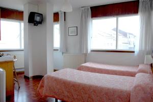 a bedroom with two beds and a tv and windows at Hostal Charo II in Santiago de Compostela