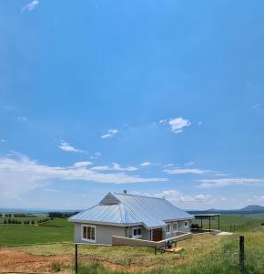 a white house with a metal roof in a field at Dragons Landing Cottage in Underberg