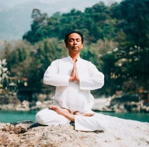 een man die op een rots zit in een meditatie houding bij Yogi Home Stay in Rishīkesh