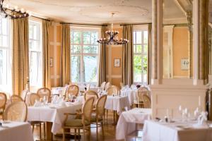 une salle à manger avec des tables blanches, des chaises et des fenêtres dans l'établissement Grand Hôtel des Rasses, à Yverdon-les-Bains
