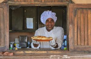 a chef holding a plate of pizza in a kitchen at Qasr El Bagawat Hotel in ‘Ezbet Halfa