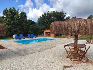 uma piscina com cadeiras e um guarda-sol de palha em Quinta do Vale em Pirenópolis