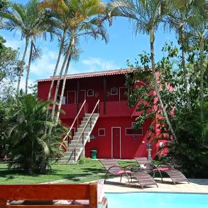 a red building with palm trees and a pool at Pousada Arpoador de Búzios in Búzios