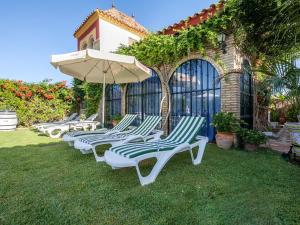 a row of lounge chairs with an umbrella on the grass at 4 bedrooms villa with private pool enclosed garden and wifi at Los Palacios y Villafranca in Los Palacios y Villafranca