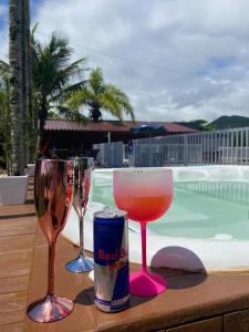 três copos de vinho e uma lata numa mesa perto de uma piscina em Morada da Praia 01 em Balneário Camboriú