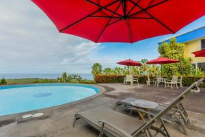 a patio with a red umbrella and chairs and a pool at Luana Inn in Captain Cook