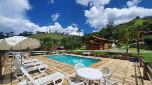 a patio with white chairs and a swimming pool at Chales Edelweiss in Visconde De Maua