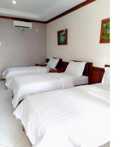 três camas num quarto de hotel com lençóis brancos em Hotel Bahtera PT.Pelni em Bogor