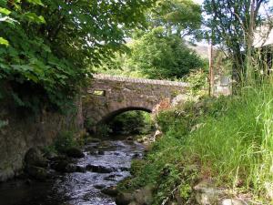un viejo puente de piedra sobre un río con un arroyo en Pen Llyn Quarryman's Cottage, en Trevor