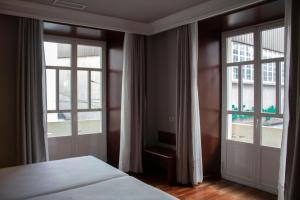 a bedroom with a bed and two large windows at Hotel Alda El Suizo in Ferrol