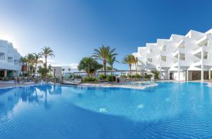 una gran piscina con palmeras y edificios en Hotel Riu Palace Jandia en Playa Jandia