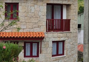 a stone building with red windows and a balcony at Casas Da Ribeira in Seia