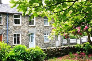 a stone house with white windows and pink flowers at Stone Cottage at Staveley in Windermere
