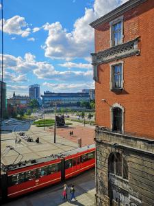 a red train traveling past a brick building next to a building at Rynek 7 in Katowice