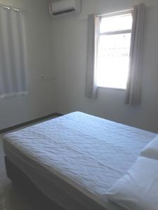a bed in a white room with a window at Casa de Temporada Guaibim in Guaibim