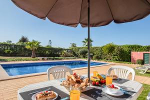 a table with food and an umbrella next to a swimming pool at Villa Sunrise by Algarve Vacation in Carvoeiro