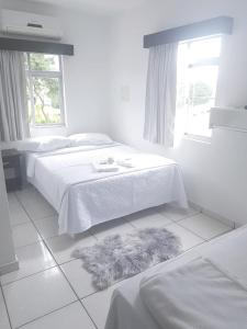 a white bedroom with two beds and a rug at Hotel Salto do Norte in Blumenau