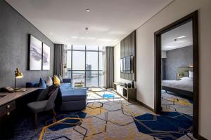 a living room with a blue couch and a bed and a desk at Pullman Sharjah in Sharjah