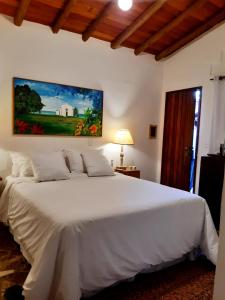 a bedroom with a white bed with a painting on the wall at Casa Rabanete Trancoso in Trancoso