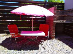 Deux chaises rouges et un parasol à côté d'un bâtiment dans l'établissement La Comarca, à Colonia del Sacramento