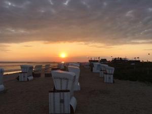 a row of chairs on the beach at sunset at Haus-Encore-Wohnung-4 in Büsum