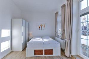 ein weißes Zimmer mit einem Bett und einem Spiegel in der Unterkunft Appartement 5 mit Südbalkon in strandnaher Lage - Bäderstil-Villa in Wenningstedt/Sylt in Wenningstedt-Braderup