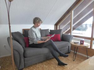 a woman sitting on a couch reading a book at Holstein-Höfle, Rindalphorn in Argenbühl