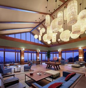 Taj Chia Kutir Resort & Spa Darjeeling في Kurseong: غرفة معيشة كبيرة مع نوافذ وثريات كبيرة