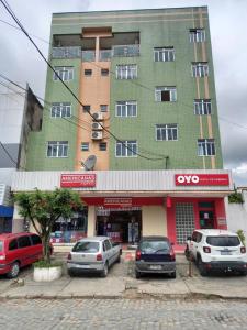 Un edificio alto y verde con coches aparcados delante. en PS Hotel Manilha, en Itaboraí