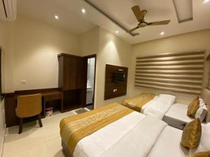 a bedroom with two beds and a desk and a television at Hotel Blossom Inn in Amritsar