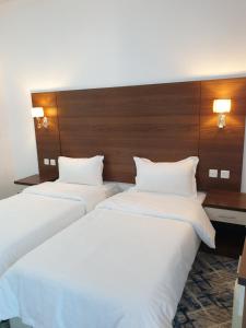 twee bedden in een hotelkamer met witte lakens bij شقق سانتوريني الخاصة Santorini Private Apartments in Al Ula