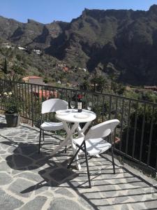 een witte tafel en 2 stoelen op een patio met bergen bij Live Masca - Estudio casas morrocatana Tenerife in Masca