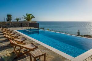 a swimming pool with chairs and the ocean in the background at Almyra Seaside Houses in Hersonissos