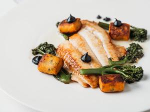 un plato blanco con un trozo de pescado y verduras en Millfields Hotel, en Grimsby