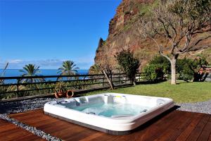 a hot tub on a wooden deck with the ocean in the background at Sunset Sea Breeze in Madalena do Mar