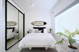 Beautifully renovated quiet unit in Cronulla في كرونولا: غرفة نوم بسرير ابيض ومرآة كبيرة