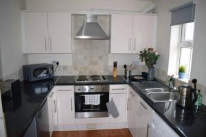 una cucina con armadi bianchi, piano cottura e lavandino di Comfortable Apartment in Sheffield with Parking a Neepsend