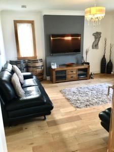 uma sala de estar com um sofá de couro preto e uma televisão de ecrã plano em Culduthel Cottage em Inverness