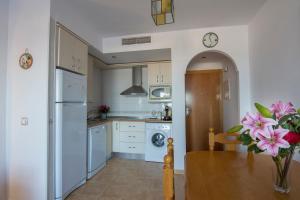 a kitchen with white appliances and pink flowers in a vase at Sunny Apartment in Mojácar