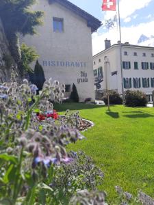 ein Gebäude mit dem Zeichen einer Universität mit Blumen im Gras in der Unterkunft Hotel Stüa Granda in Soglio