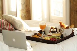 a tray of food and a laptop on a bed at 1872 River House by Olivia in Porto