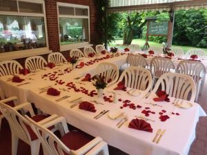 a long table with white chairs and red flowers on it at Gasthof Bathmann in Loxstedt