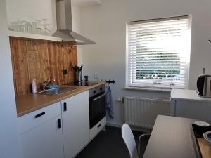a kitchen with white cabinets and a sink and a window at De Stoof, complete studio voor 2 personen in Renesse