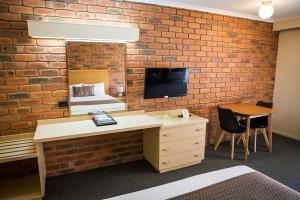 a room with a brick wall with a bed and a desk at Australian Settlers Motor Inn in Swan Hill