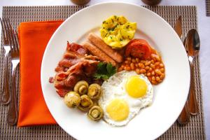 a white plate of breakfast food with eggs bacon and mushrooms at Ngorongoro Marera Mountain View Lodge in Karatu